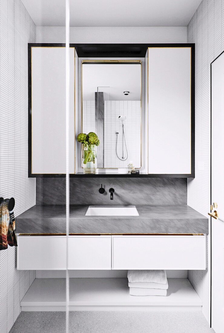 Badezimmereinbau mit marmorierter Waschtischplatte und weißem Hängeschrank mit schwarzem Rahmen