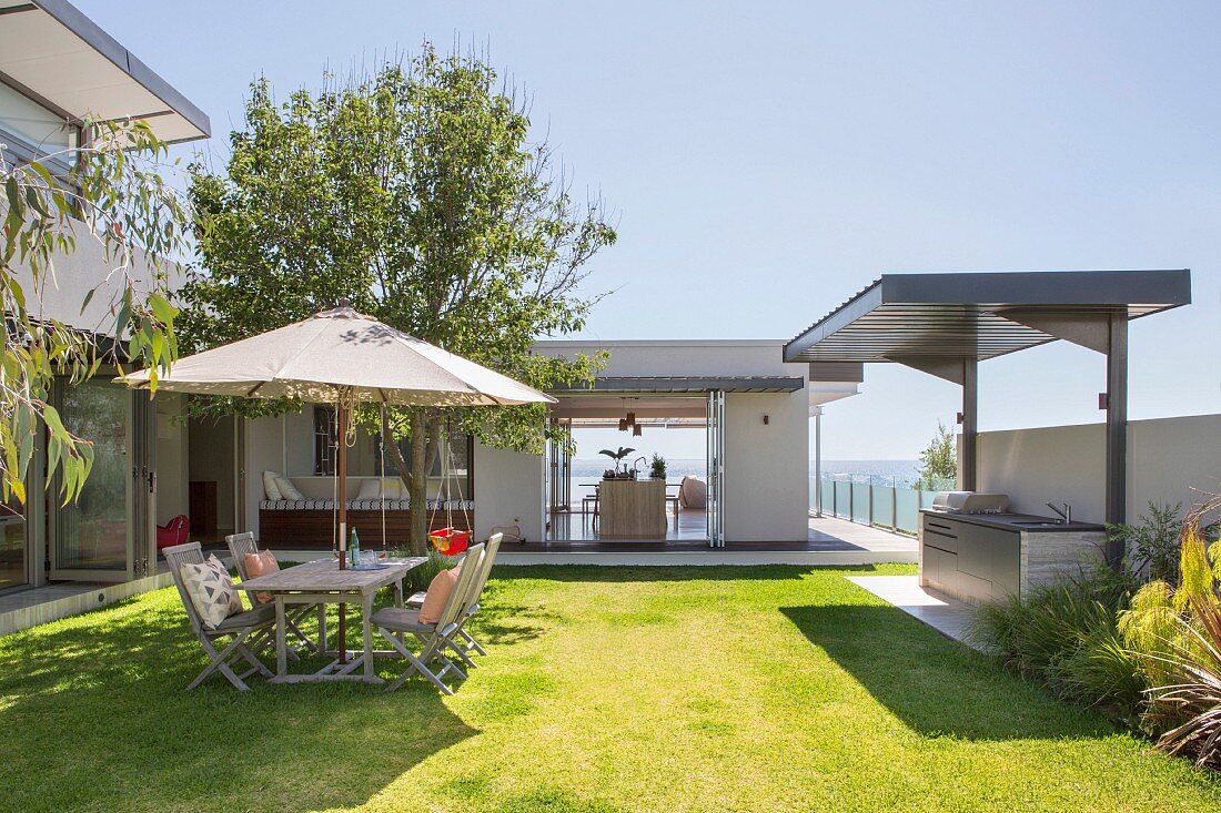 Architect's house with garden, seating under a parasol on the lawn, outdoor kitchen and sea view