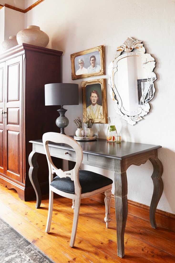 Rokoko Schreibtisch mit Tischleuchte und Stuhl vor Wand mit geramhten Bildern und Speigel