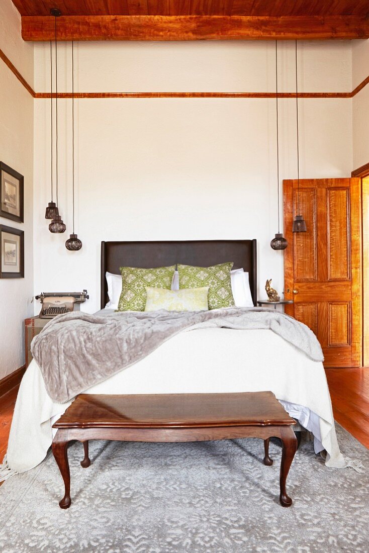 Double bed and bedroom bench made from exotic wood in high-ceilinged bedroom with pendant lamps