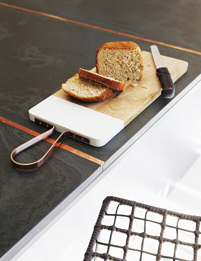 Schneidebrett mit Brot und Messer auf anthrazitfarbener Küchenarbeitsplatte
