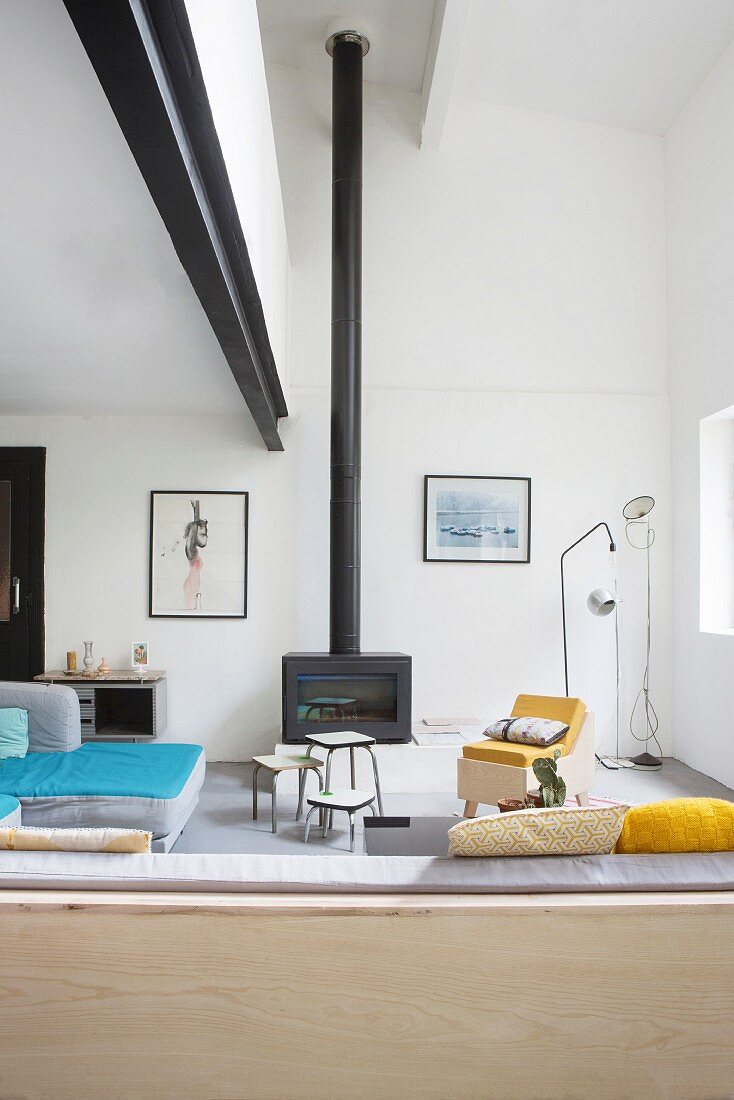 Black steel girder and wood-burning stove with tall stove pipe in eclectic living area