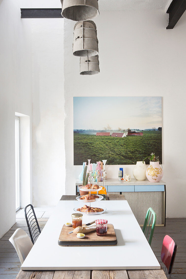 Rustikaler Esstisch mit weisser, aufgelegter Tischplatte vor Fotokunstbild und Vasensammlung