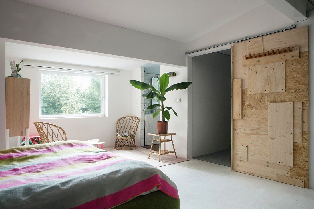 Schlafzimmer mit DIY-Schiebetür aus verschiedenen Holzplatten, und Grünpflanze auf Naturrohr-Tischchen