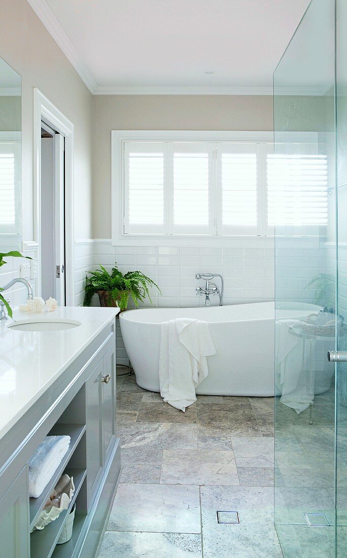 Elegant bathroom with free-standing white bathtub, natural stone tile floor and green plants