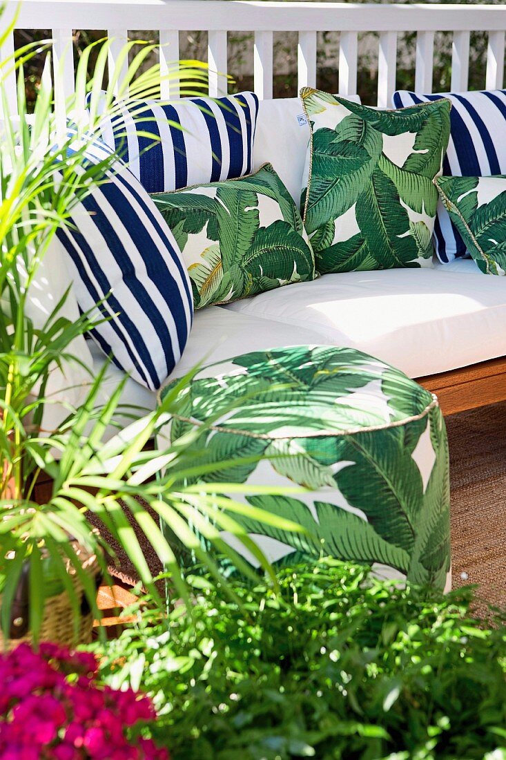Sonnige Terrasse mit Grünpflanzen, Sitzpouf und gemütlichem Polstersofa mit verschiedenen Kissen