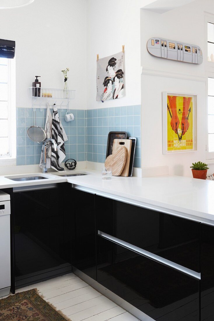 Black fitted kitchen units with white worksurface and splashback of pale blue wall tiles