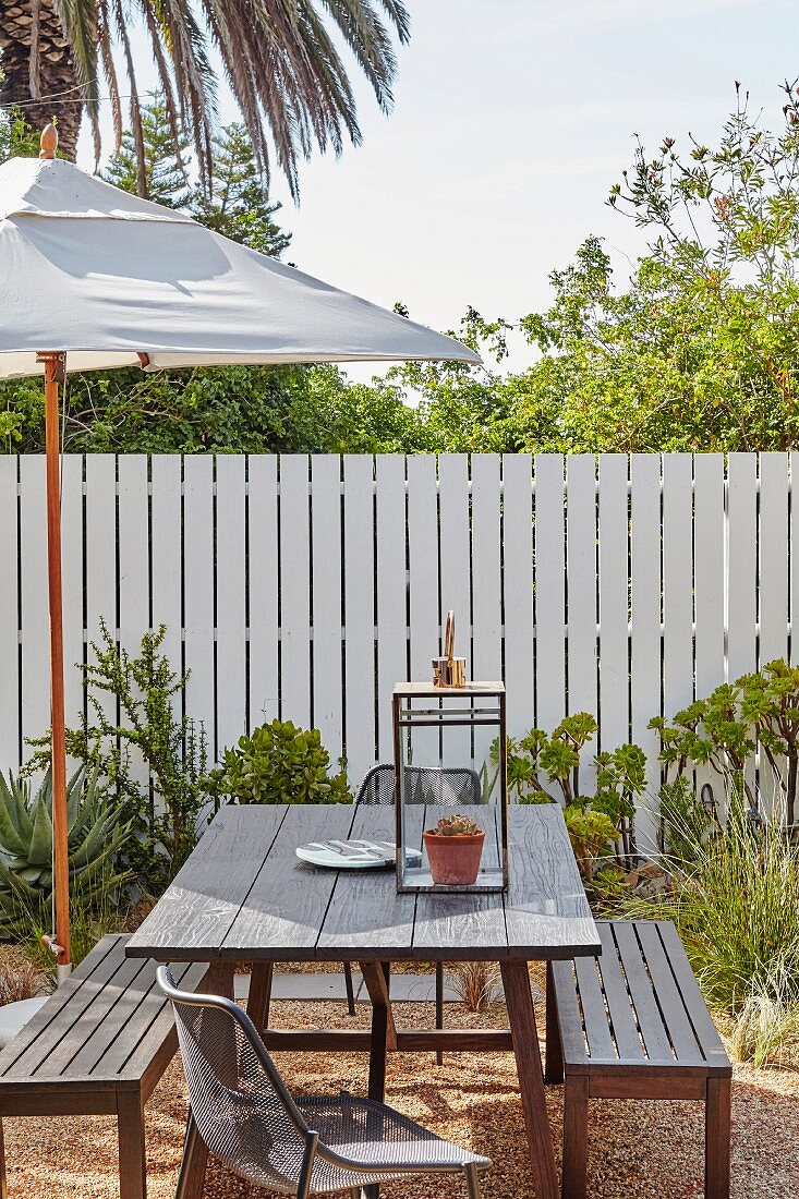 Parasol and wooden outdoor furniture on terrace in front of picket fence