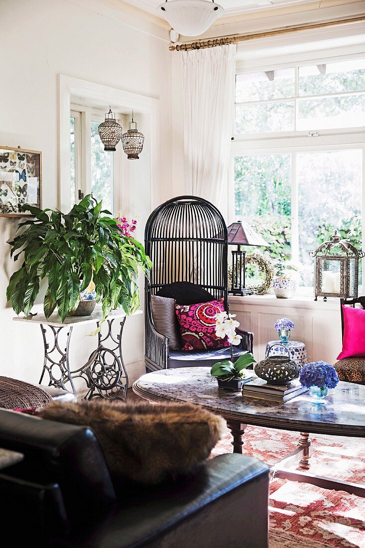 Black wicker chair next to nostalgic sewing machine table with green plants in living room with ethnic flair