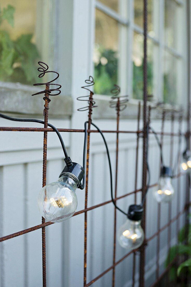 Einfache Lichterkette an rostigem Metallgitter vor Holzfassade