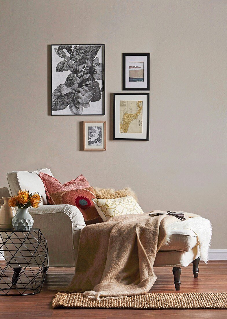 Cozy chaise longue with pillows and woolen blanket against beige wall with picture gallery