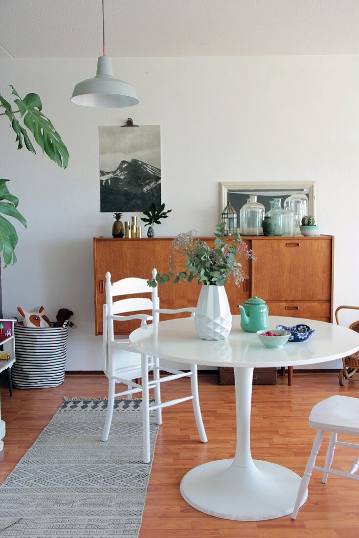 Round table and white high chair in front of retro sideboard