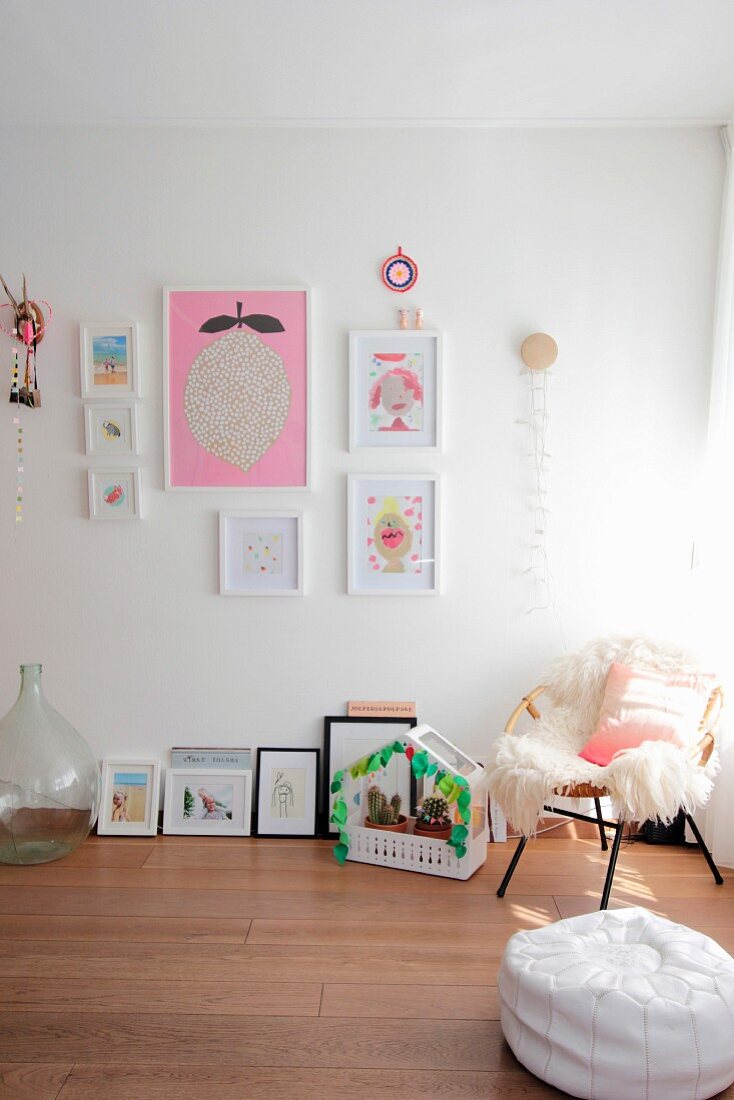 Pale sheepskin and pink cushion on wicker chair next to various child's drawings and cacti in small house