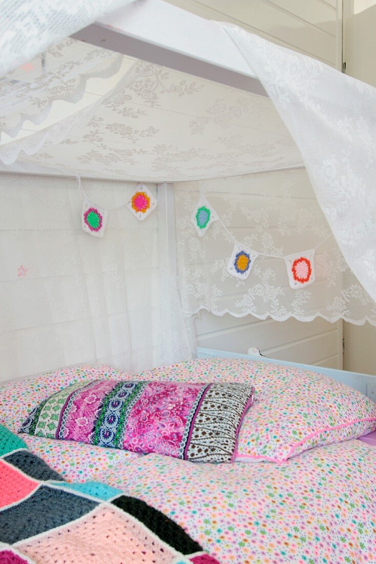 Colourful crocheted garland and pastel bed linen on pretty bed with white canopy in girl's bedroom