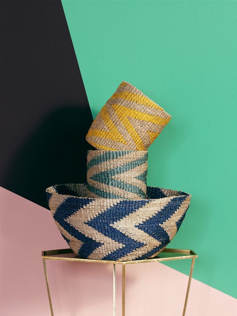 Woven baskets with zigzag patterns against wall with geometric pattern of bright colours