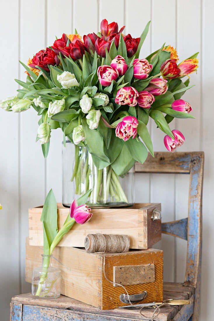 Opulent bouquet of tulips of various colours on stacked wooden crated on chair