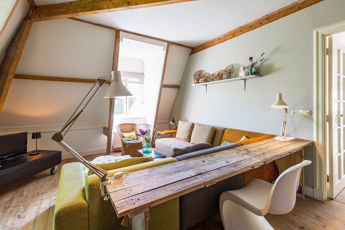 Klassiker Schalenstuhl und selbstgebauter Tisch vor gemütlicher Polstercouch übereck im Dachzimmer