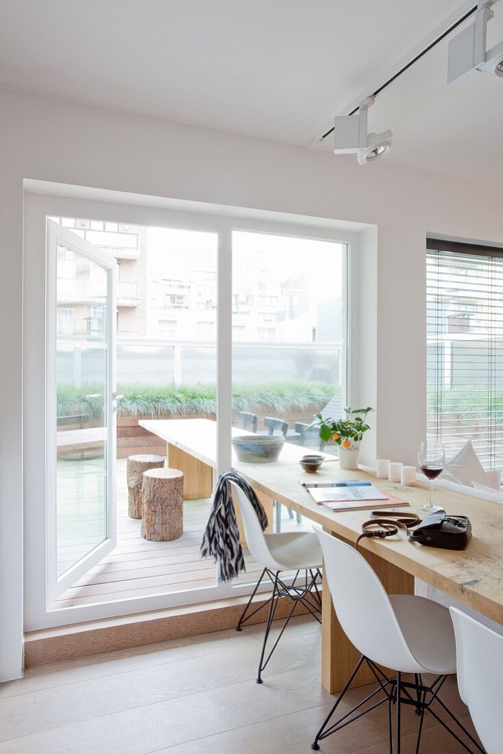 Long wooden dining table and white classic chairs next to terrace window