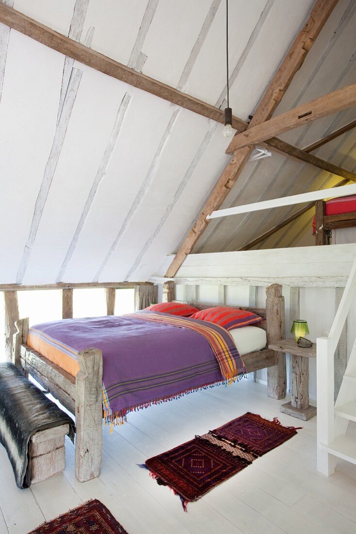 Rustikales Doppelbett aus Holz in Schlafraum mit weißem Dielenboden unter dem Dach