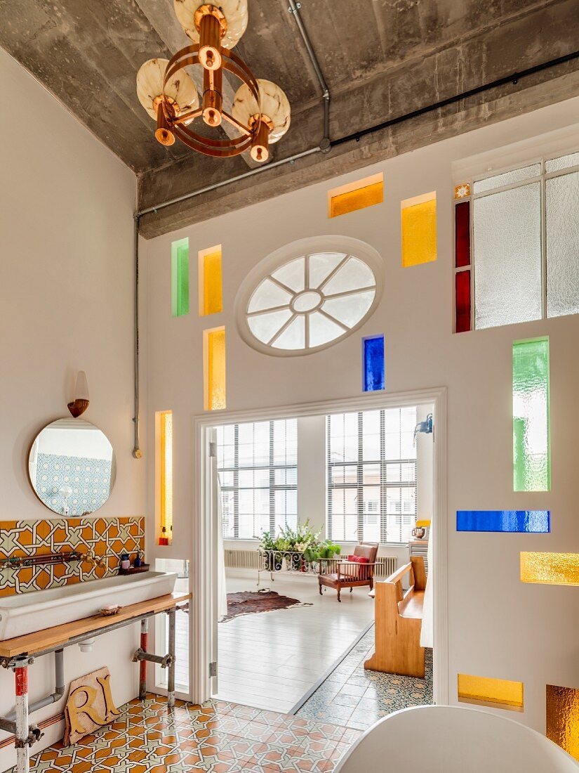 Modern stained-glass elements in partition wall between vintage-style bathroom and open-plan living area in loft apartment