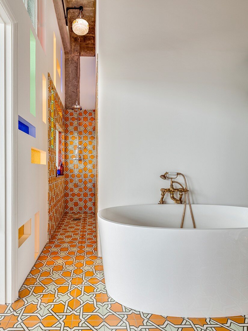 Freistehende, moderne Badewanne vor weisser Wand und Duschbereich mit Ornamentfliesen