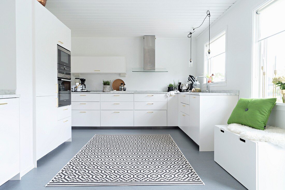 Elegante, weiße Einbauküche mit Sitztruhe unter dem Fenster, Teppich mit grafischem Muster