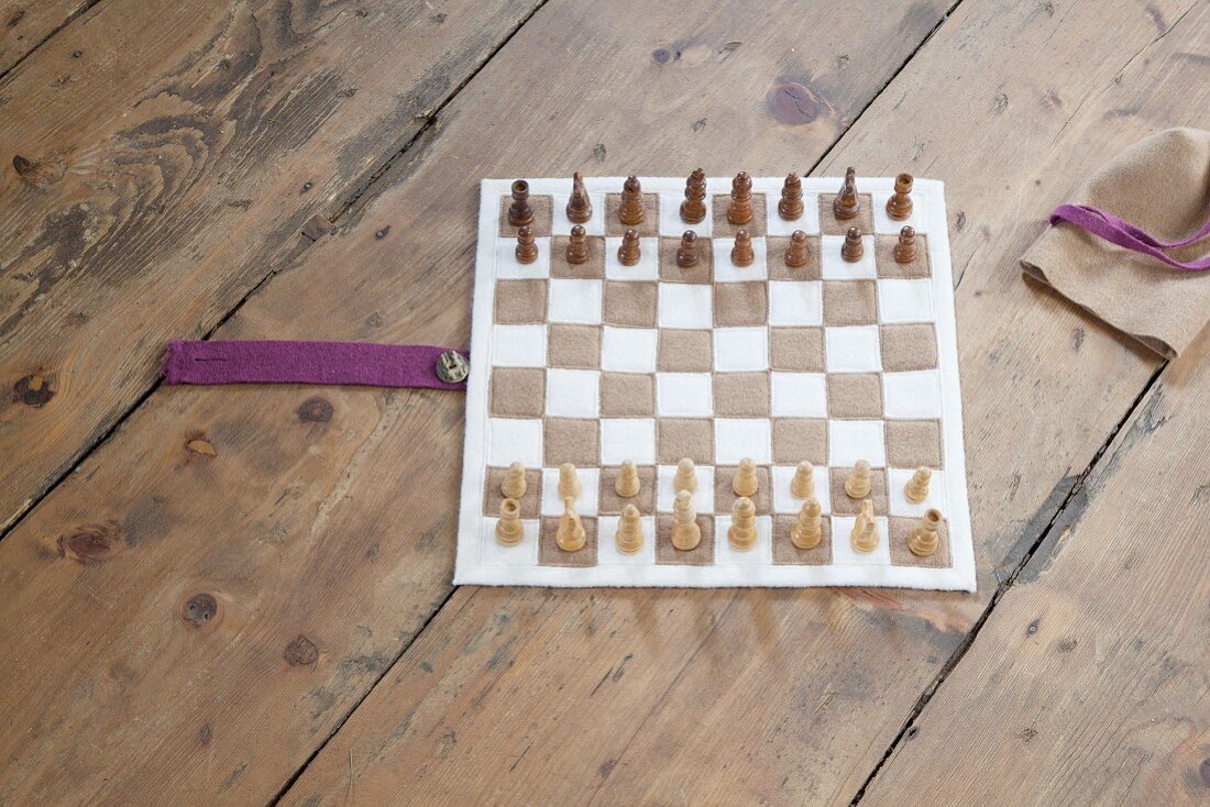 Hand-sewn boiled-wool chessboard and wooden chess pieces on rustic wooden floor