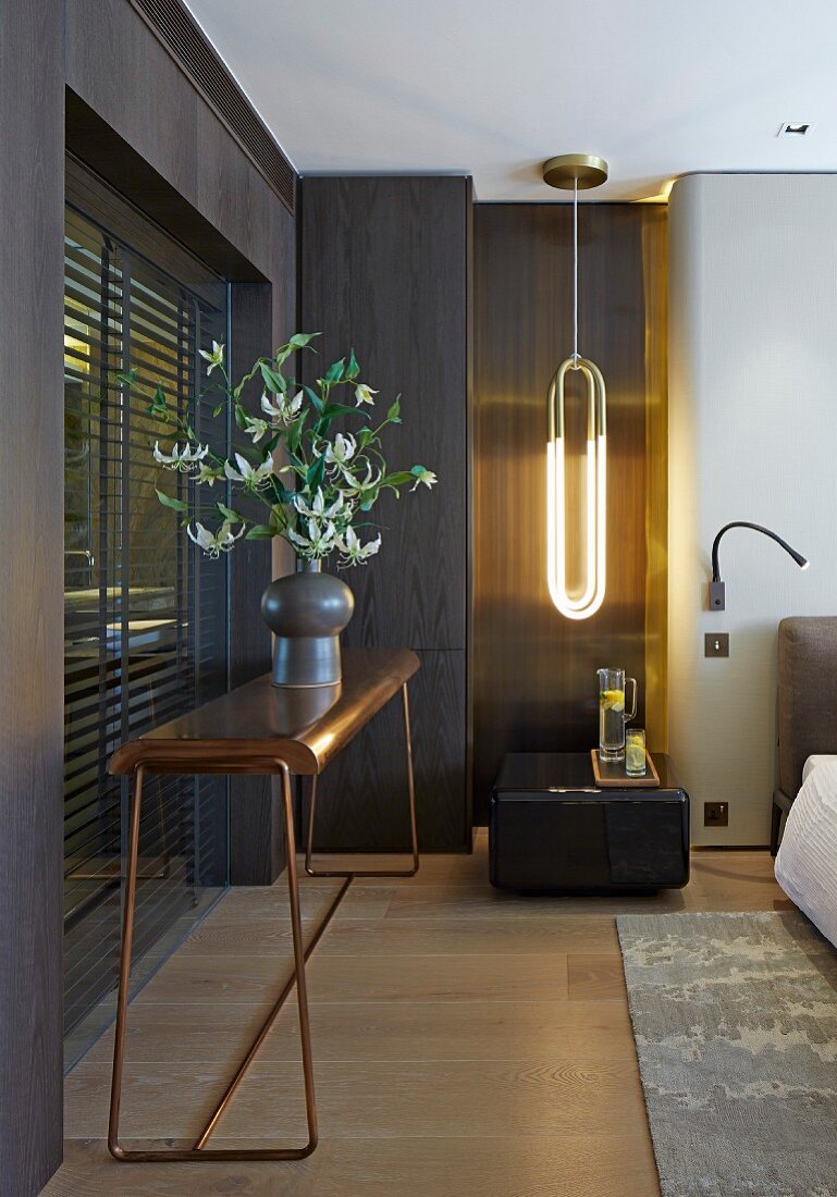 Vase of flowering branches on metal console table and pendant lamp above side table in bedroom