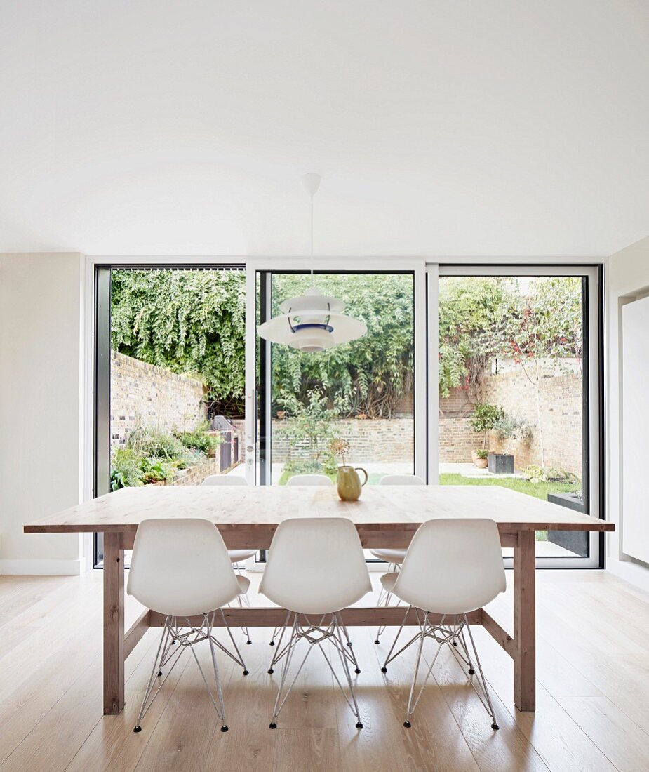 White classic shell chairs around wooden table in front of glass sliding doors