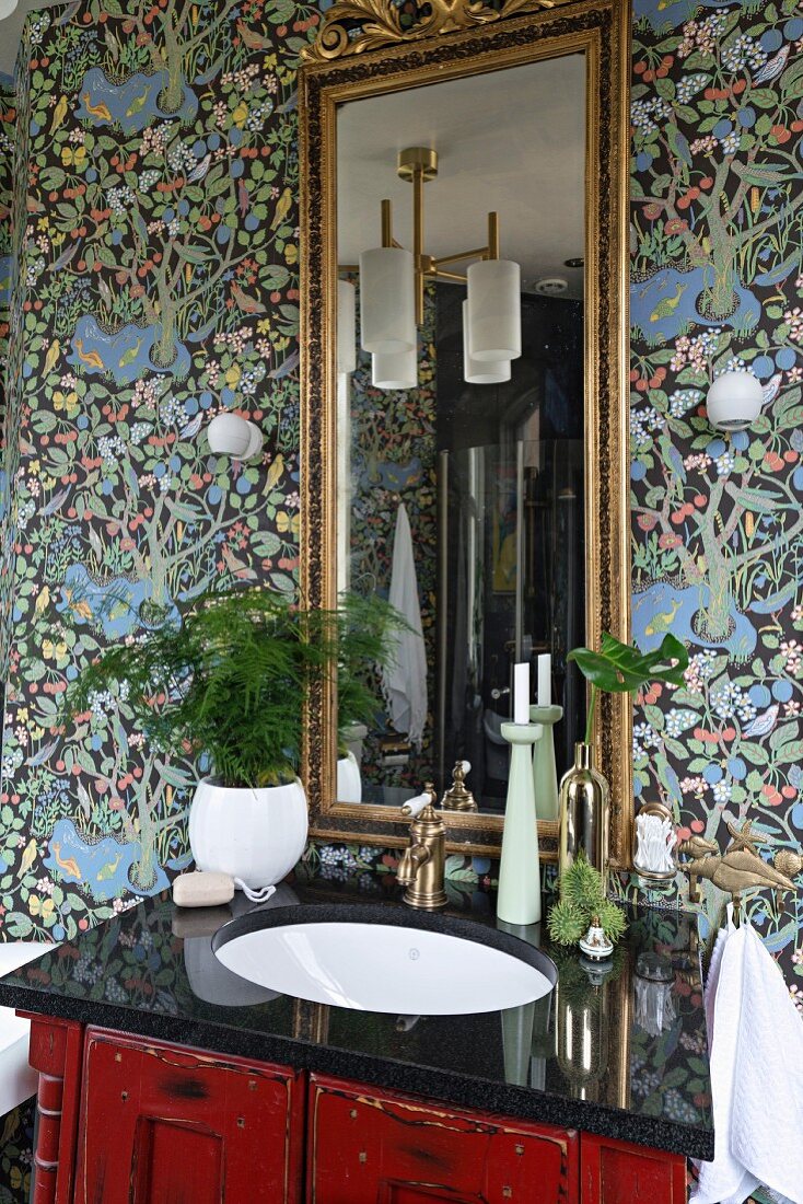 Vintage Waschtisch mit schwarzer, polierter Platte, darauf Grünpflanze vor Wandspiegel mit Goldrahmen