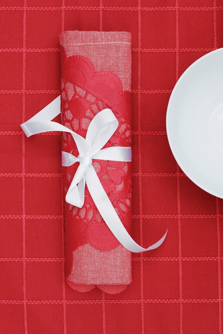 Rote Stoffserviette und Spitzenpapier mit weißem Schleifenband auf roter Tischdecke