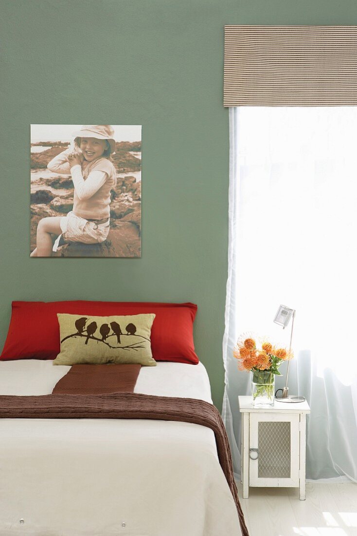Bett mit drapierten Kissen und Tagesdecke vor grün getönter Wand