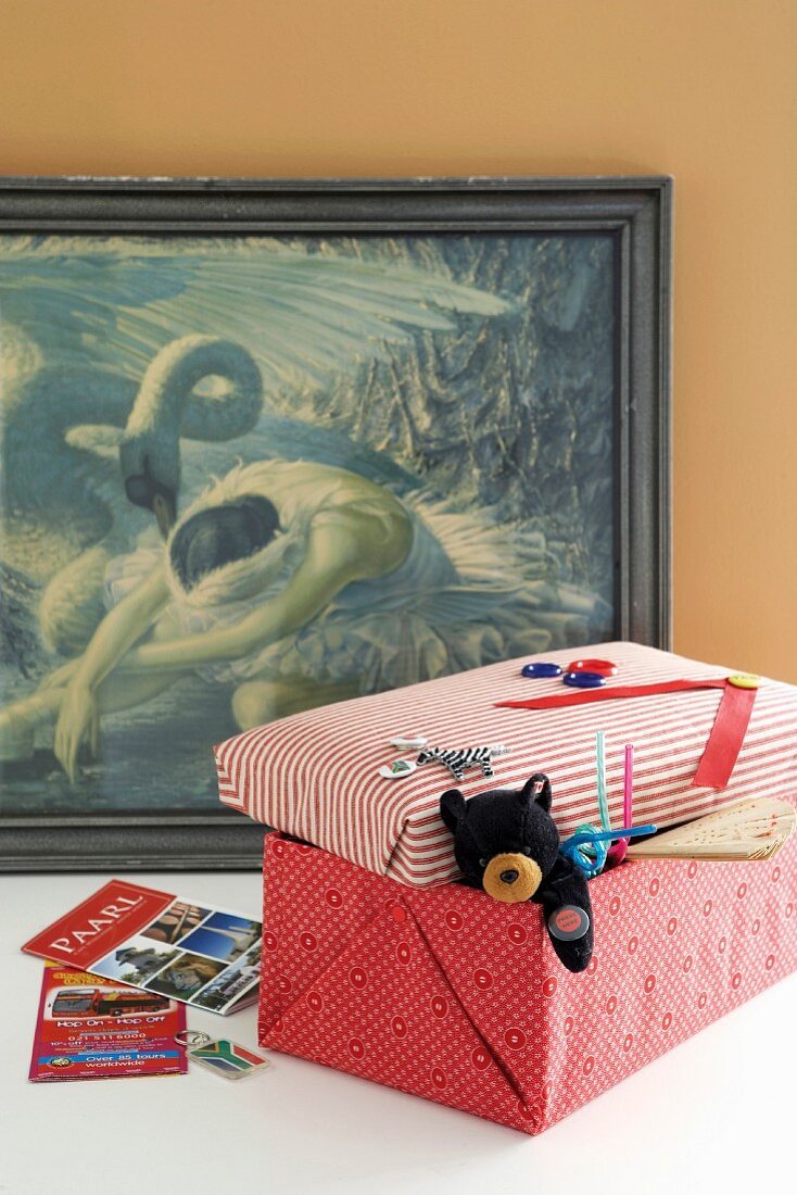 Toy box covered in colourful paper in front ot framed picture of swan and ballerina