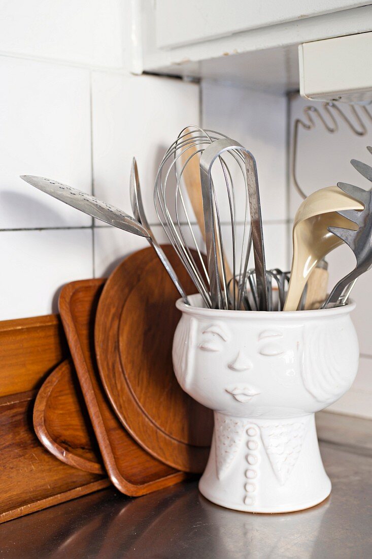 Kitchen utensils in face pot in front of wooden plates