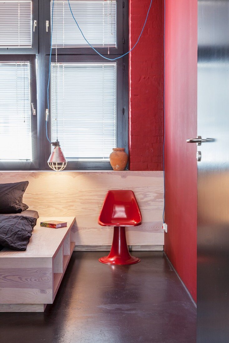 Blick in Schlafzimmer mit massgefertigtem Betthaupt und rotem, glänzendem Stuhl