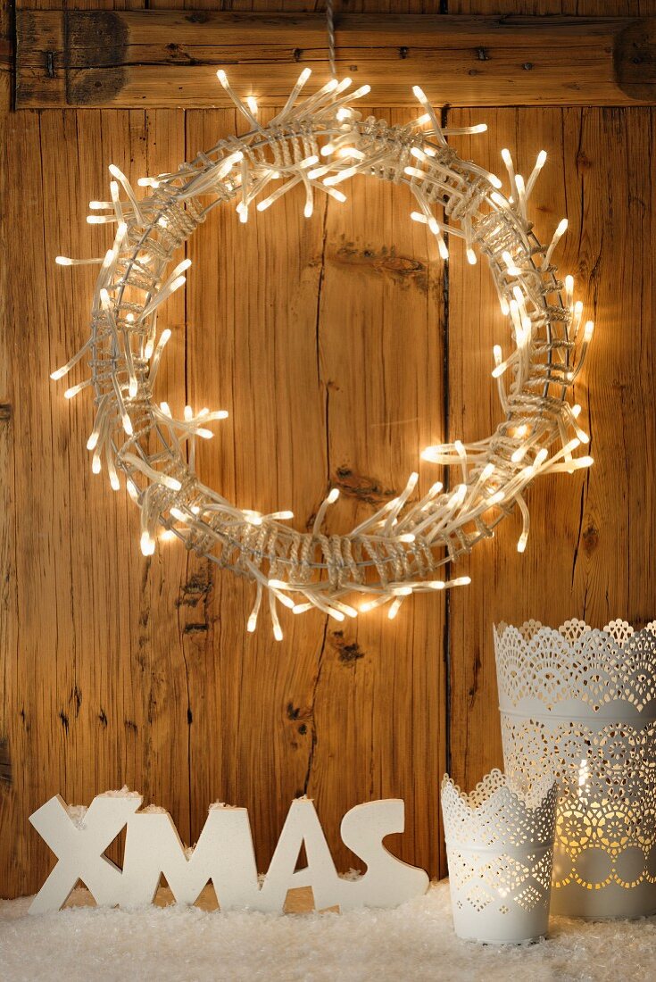 White Christmas arrangement below wreath of lights on wooden wall