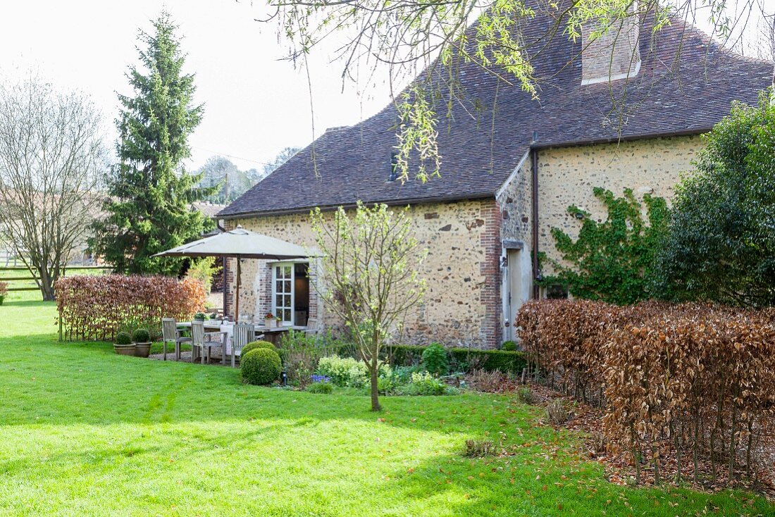 Idyllisches, traditionelles Cottage mit grüner Rasenfläche und Frühlings-Blumenbeet