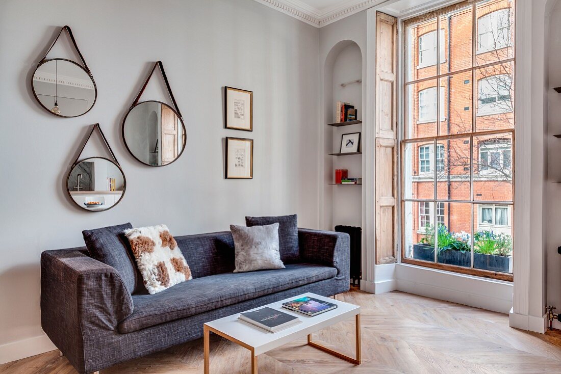 Three mirrors above grey sofa in renovated townhouse apartment