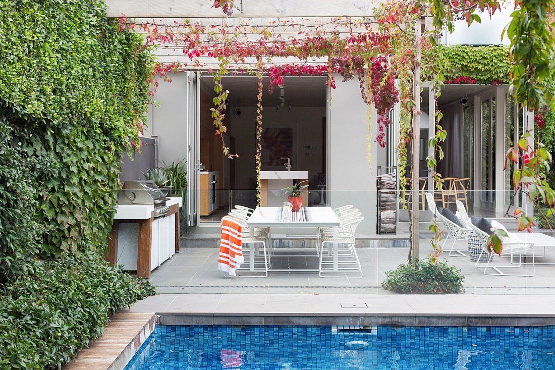 Pool mit Glasbrüstung vor Terrassenplatz mit Outdoor-Küche und Lounge