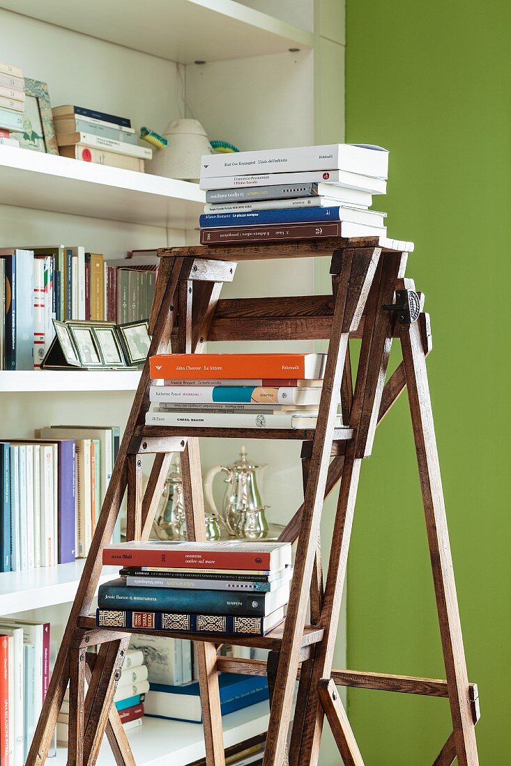 Books stacked on wooden ladder in front of bookcase