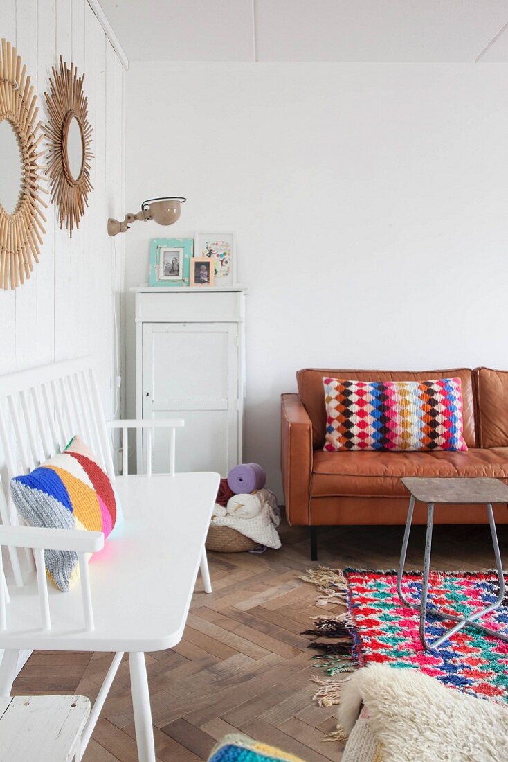 White wooden bench and colourful crocheted cushions on leather couch in living area
