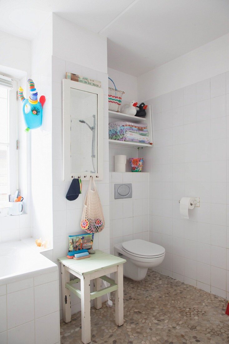 Weisses Bad mit Kieselsteinboden, Toilette, Holzhocker und Wandspiegel
