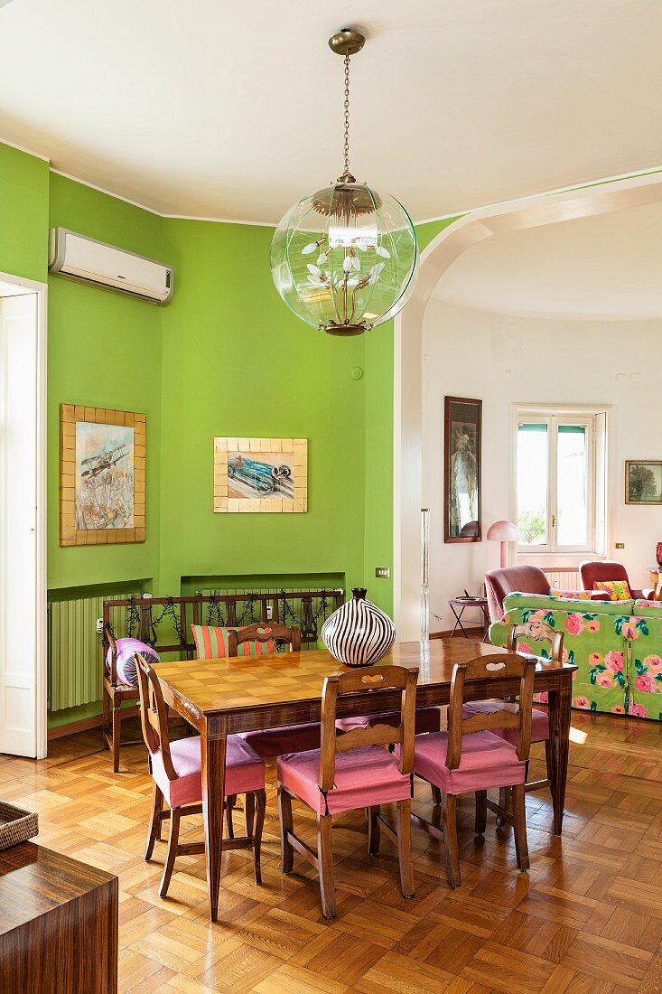 Dining table, wooden chairs and green walls in front of open doorway leading into living room