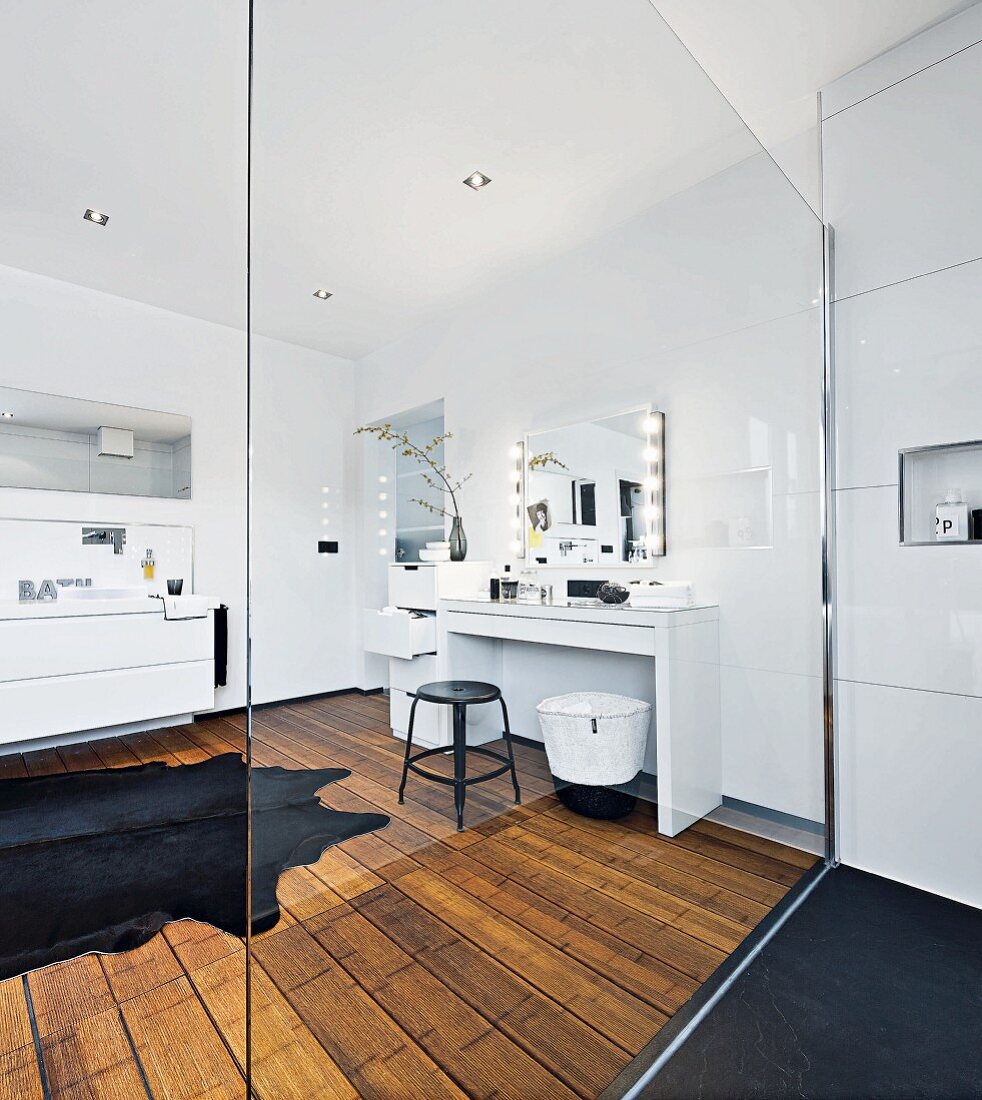 A modern white bathroom with a make-up table and a shower area with a glass panel