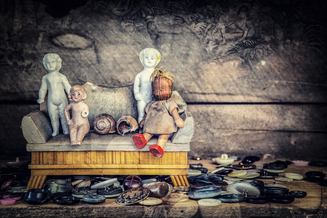 Collection of buttons and various antique dolls sitting on dolls' couch against dark background
