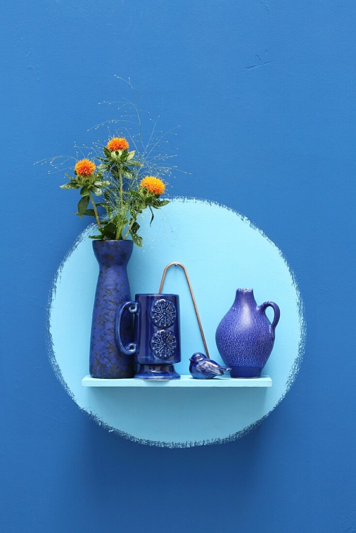 Keramikgefäße mit Blumenstrauß auf Wandboard vor hellblauem Kreis auf blauer Wand