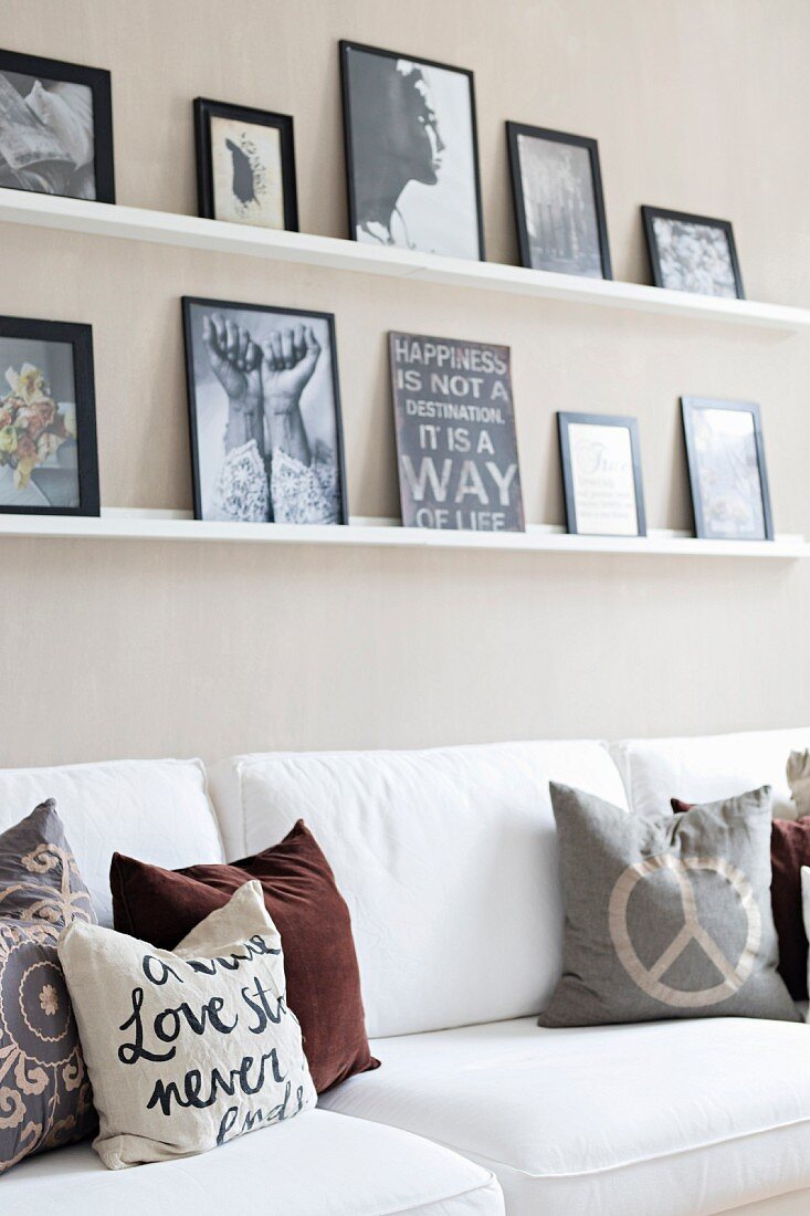 Scatter cushions in earthy tones on white sofa below pictures on narrow shelves