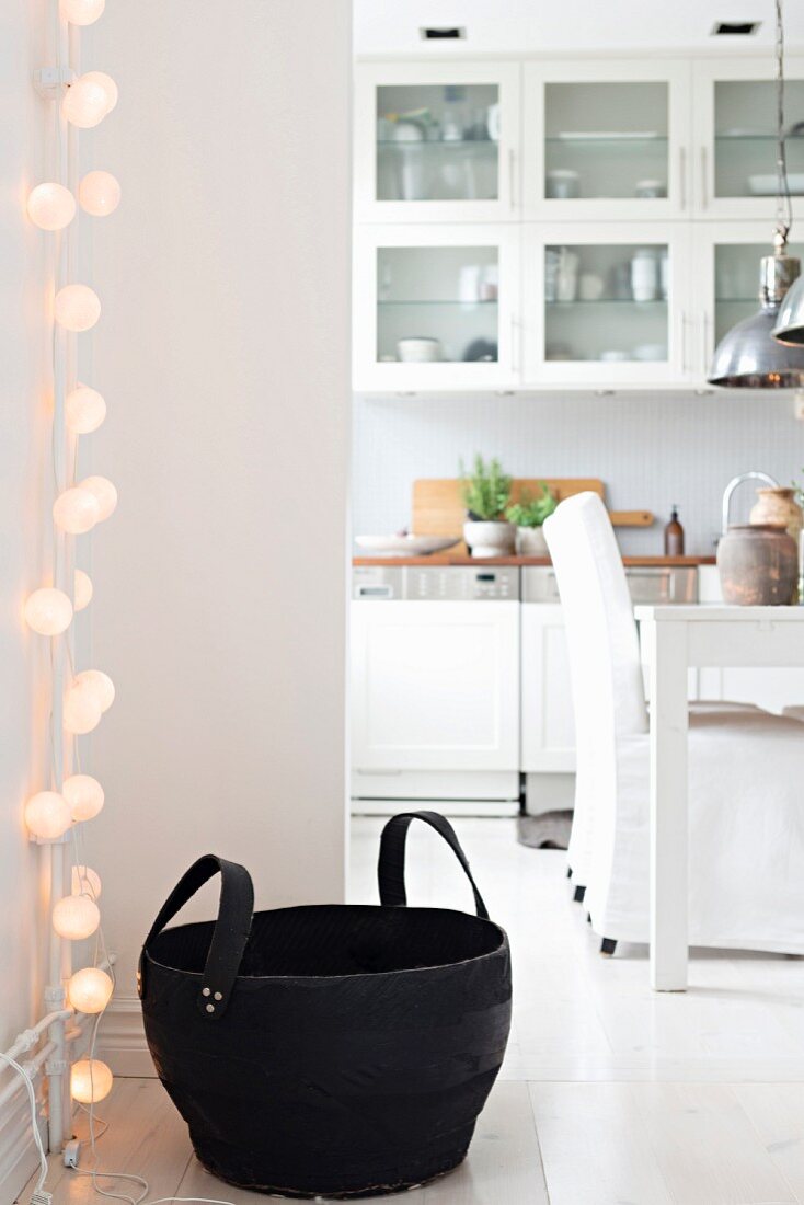 Lichterkette und schwarzer Korb vor offener Küche mit Essplatz