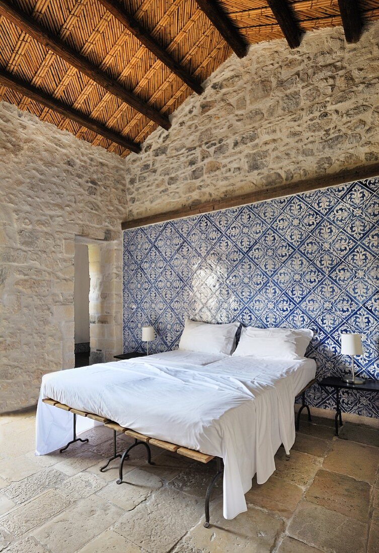 Schlafzimmer mit blau-weißen Wandfliesen in restauriertem Altbau mit Natursteinboden