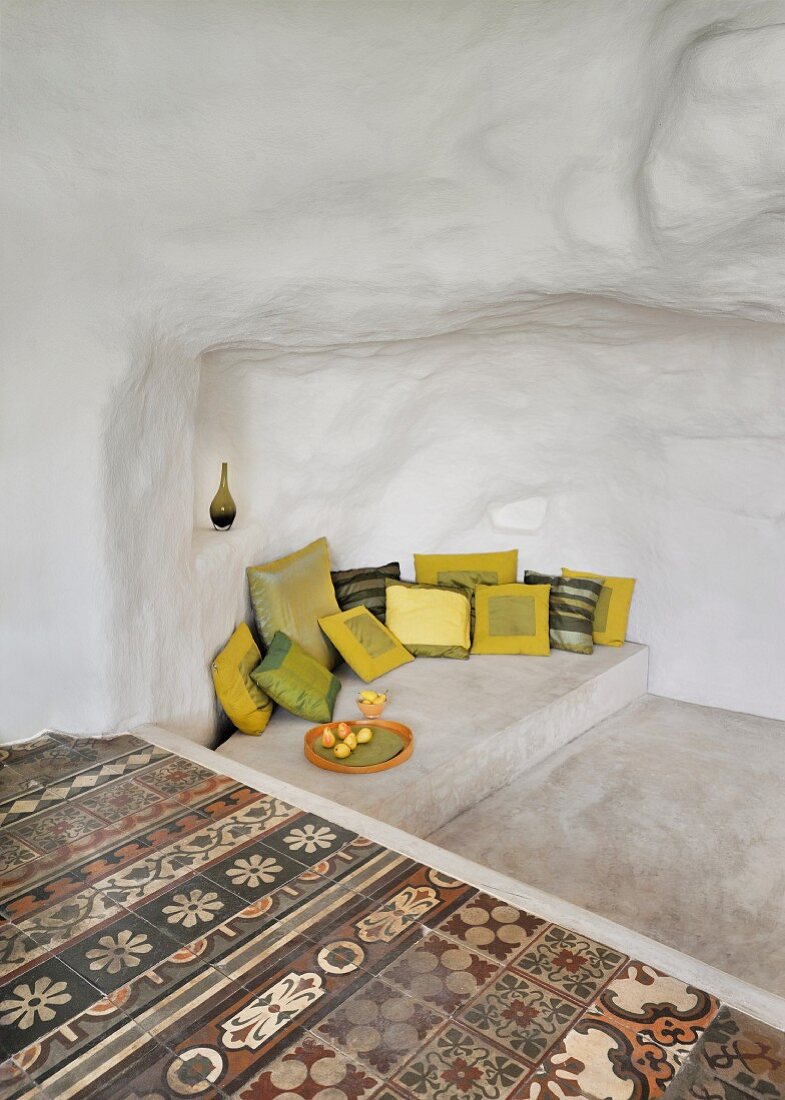 Betonpodest mit verschiedenen Kissen neben traditionellen Bodenfliesen in höhlenartigem Ambiente
